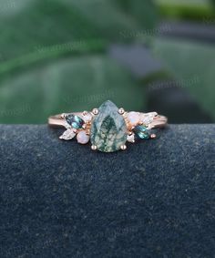 a green and white stone ring on top of a black surface with leaves in the background