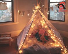 a teepee with fairy lights on it in front of two windows