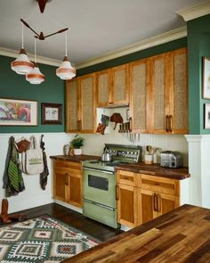 a kitchen with green walls and wooden cabinets, an oven, sink, and rug