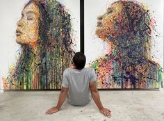 a man sitting on the floor in front of two large paintings with different colors and shapes