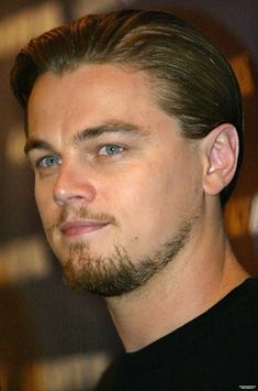 a close up of a man with a beard and blue eyes wearing a black shirt