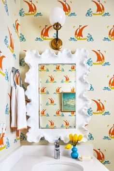 a bathroom sink with a mirror above it and wallpaper behind it, along with a towel rack