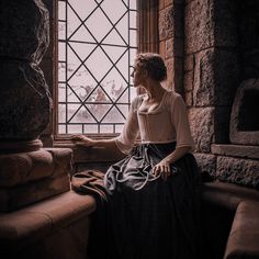 a woman sitting on a window sill in front of a stone building with a stained glass window