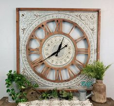 a clock sitting on top of a wooden table next to potted plants and a lace doily