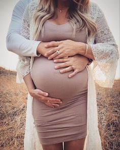 a pregnant woman is holding her belly while standing in a field