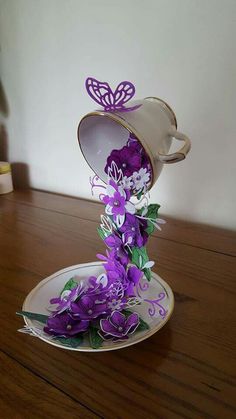 purple flowers in a teacup on a plate with a butterfly sitting on top of it