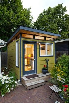 a small yellow and blue shed in the middle of a yard with flowers around it