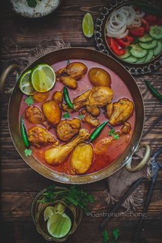 a pan filled with chicken and vegetables next to sliced cucumbers on a wooden table