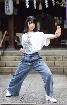 a woman in jeans and a white t - shirt is doing a dance move on the street