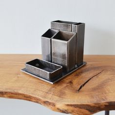 three square metal containers sitting on top of a wooden table next to a planter