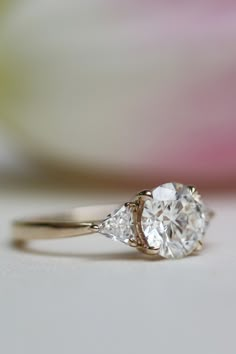 an engagement ring with two pear shaped diamonds on it and a flower in the background