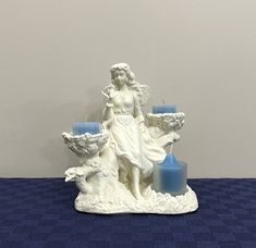 a white statue with blue candles in front of it on a blue tableclothed surface