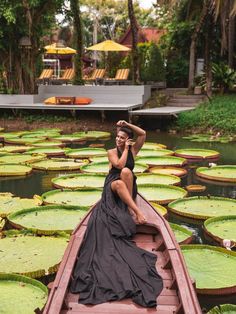 a woman sitting on the back of a boat in a pond filled with lily pads