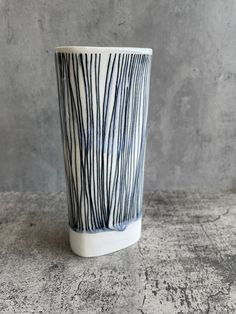 a white and blue vase sitting on top of a cement floor next to a wall