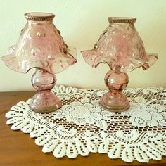 two pink glass lamps sitting on top of a doily next to a white wall