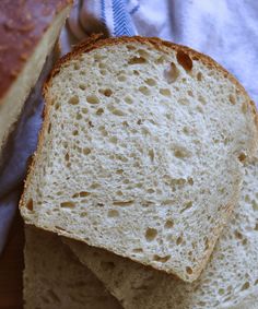 two pieces of bread sitting on top of a white towel next to a loaf of bread