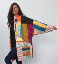 a woman wearing a multicolored jacket and jeans is holding her arms out to the side