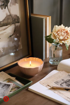 a table topped with a vase filled with flowers next to a lit candle and books