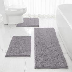 three bathroom rugs on the floor in front of a toilet and bathtub with white walls