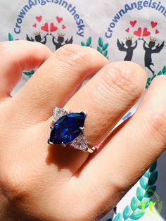 a woman's hand holding a blue ring with two diamonds on it and an emblem in the background