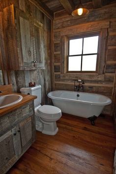 a bathroom with wooden walls and flooring has a bathtub, toilet, and sink