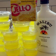 several plastic cups filled with yellow liquid next to a bottle of jello