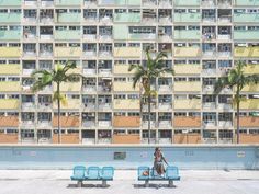 a person sitting on a bench in front of a building with balconies and palm trees