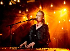 a woman is playing the keyboard in front of microphones and lights on a stage