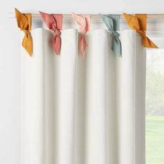 four different colored bows hanging from the top of a window curtain in front of a window