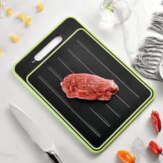 a piece of raw meat on a cutting board next to knifes and peppercorst