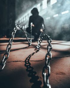 a person sitting on the ground in front of a metal chain with chains attached to it