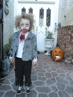 a young child dressed as a zombie standing in front of a house with pumpkins