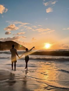 a man and woman holding hands while walking on the beach at sunset with their arms around each other