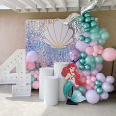 the little mermaid balloon arch is set up for a birthday party with pink, blue and green balloons