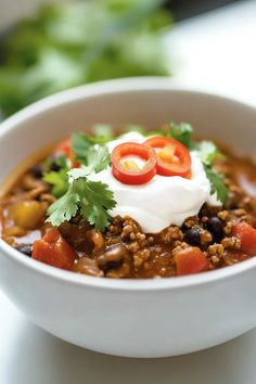 a white bowl filled with chili, beans and sour cream topped with cilantro