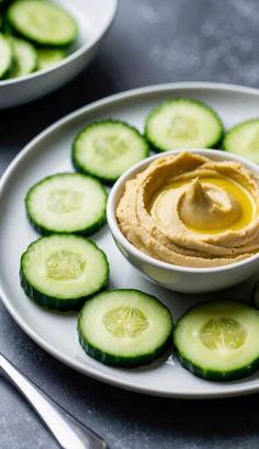 a plate with cucumber slices and hummus on it next to a bowl of dip