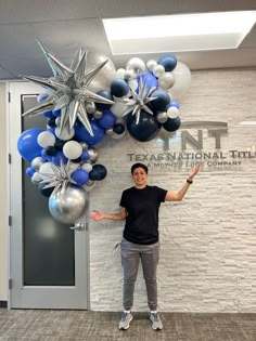 a man standing in front of a wall with blue and silver balloons hanging from it