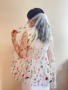 a woman wearing a veil with flowers and butterflies on it, standing in front of a wall