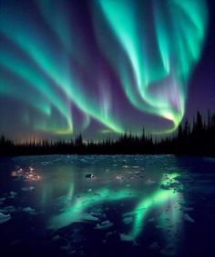 the aurora bore is shining brightly in the night sky over an icy lake and forest