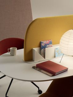 a table with a book, lamp and cup on it next to a chair in the background