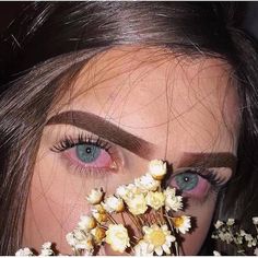 a woman with blue eyes holding flowers in front of her face