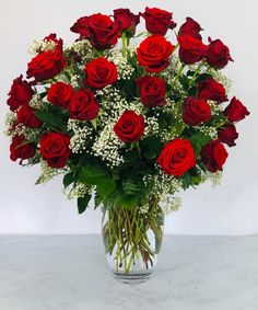 a vase filled with red roses and white baby's breath on a marble surface