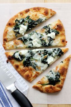 four slices of pizza with cheese and spinach on a cutting board next to a knife