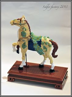 a toy horse made out of legos sitting on top of a wooden base with a white background