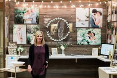 a woman standing in front of a table with pictures on it and lights hanging from the ceiling