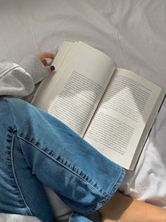 a person laying on a bed with an open book in their lap and reading it