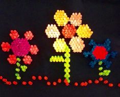 several different colored beads are arranged in the shape of flowers on a black surface with red, yellow, and green dots