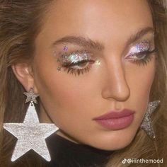 a close up of a woman with glitter on her face and star shaped earring