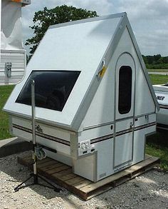 a small white trailer sitting on top of a parking lot next to a parked car