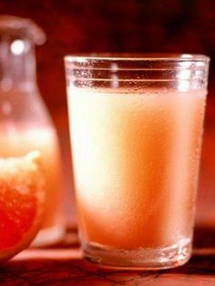 a glass filled with liquid next to a grapefruit and a bottle on a table